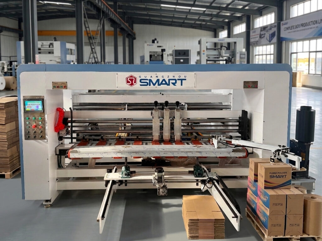 Front view of a flexo folder gluer machine in a cardboard manufacturing plant with stacked finished corrugated boxes.